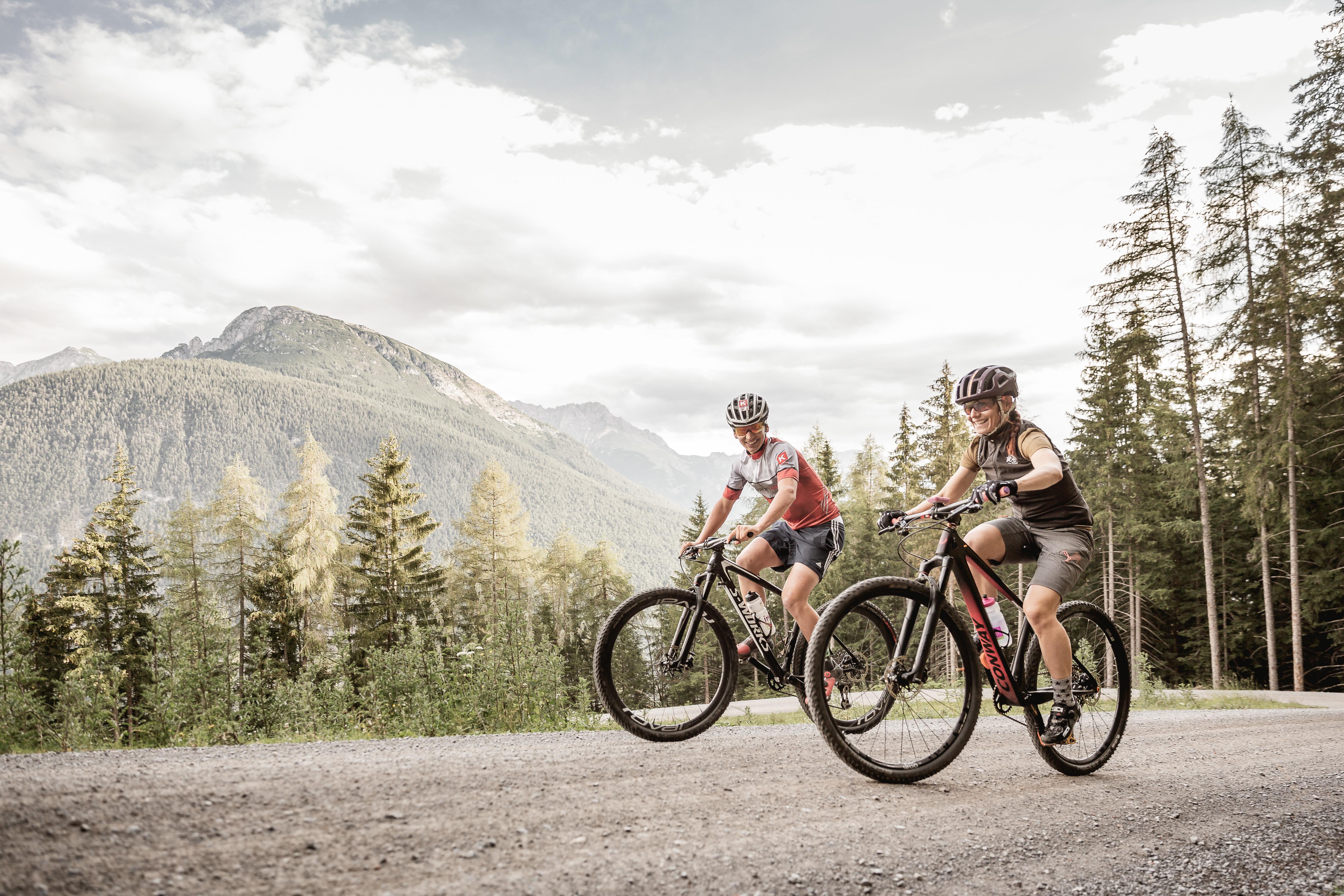 Mann und Frau fahren Mountainbike mit Alpen und Wald im Hintergrund