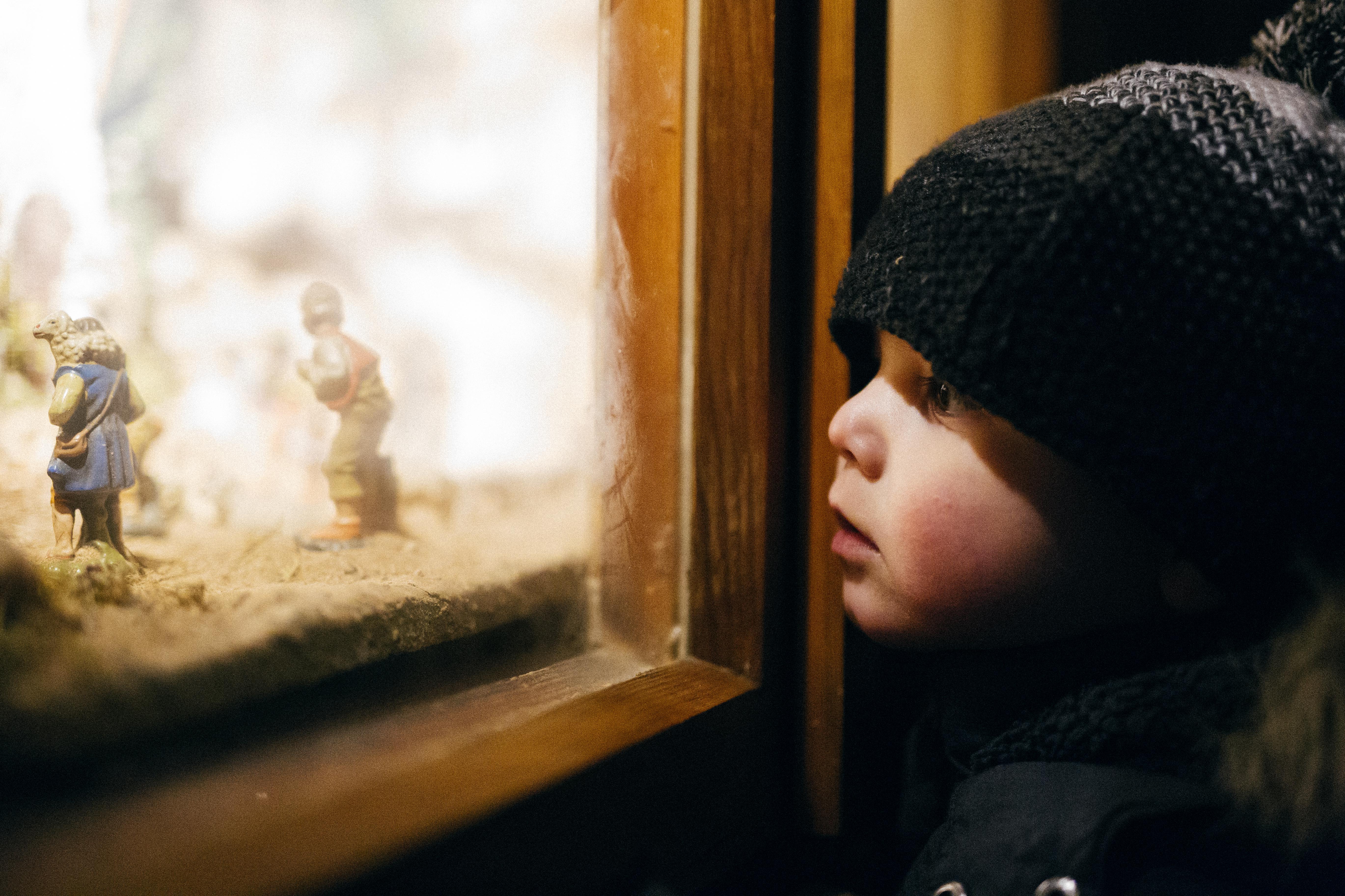 Kleiner Junge mit Mütze schaut auf Krippe im Fenster