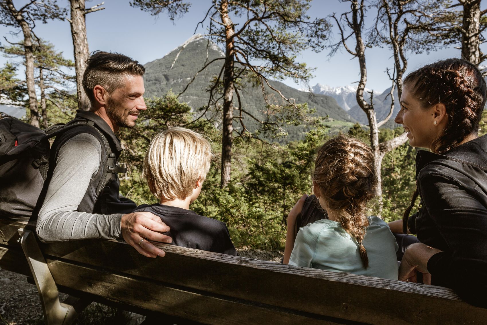 Blick von hinten auf Familie die auf Bank in Natur sitzt 