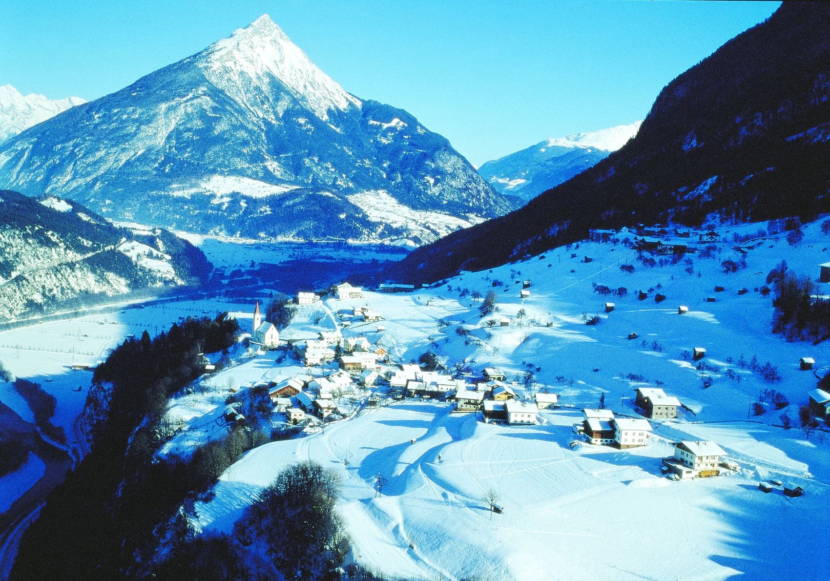 schneebedecktes Tal mit Dorf und Berg mit schneebedecktem Gipfel