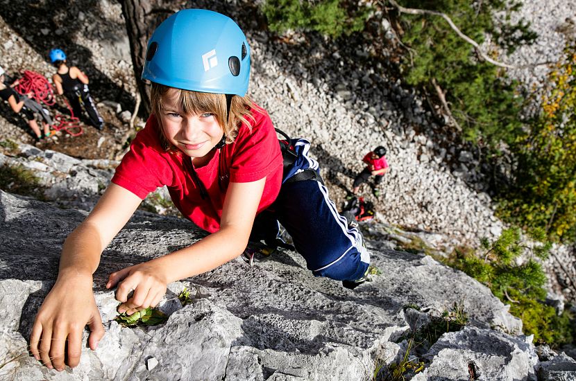 A boy climbs on a rock while being secured with a rope.