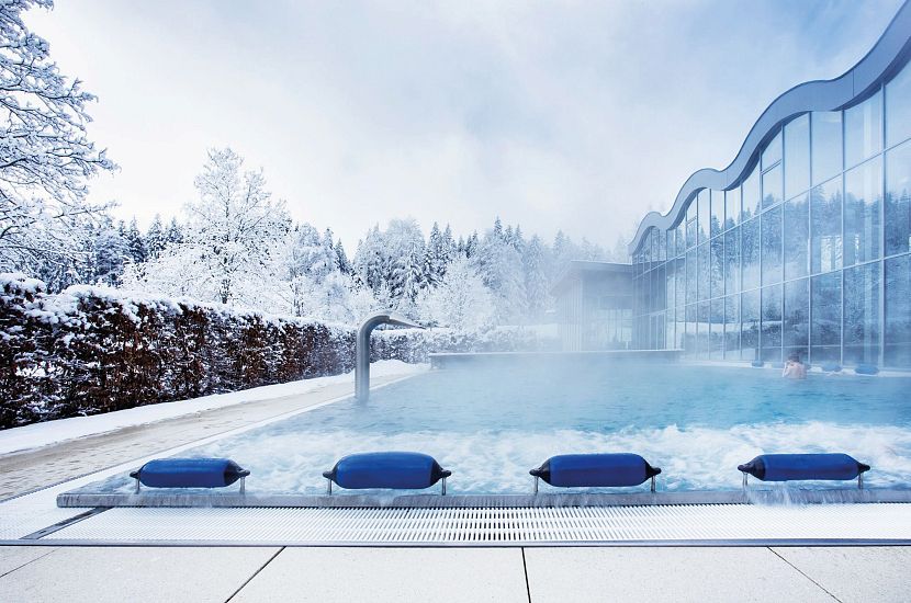 The outdoor pool at Alpenbad Leutasch surrounded by snow-covered trees