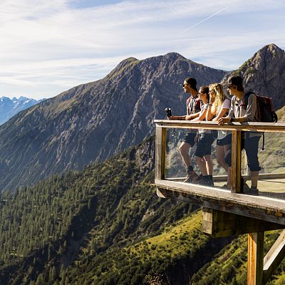 Eine Panorama-Terrasse aus Holz auf der vier Wanderer die Aussicht auf die Berge genießen.