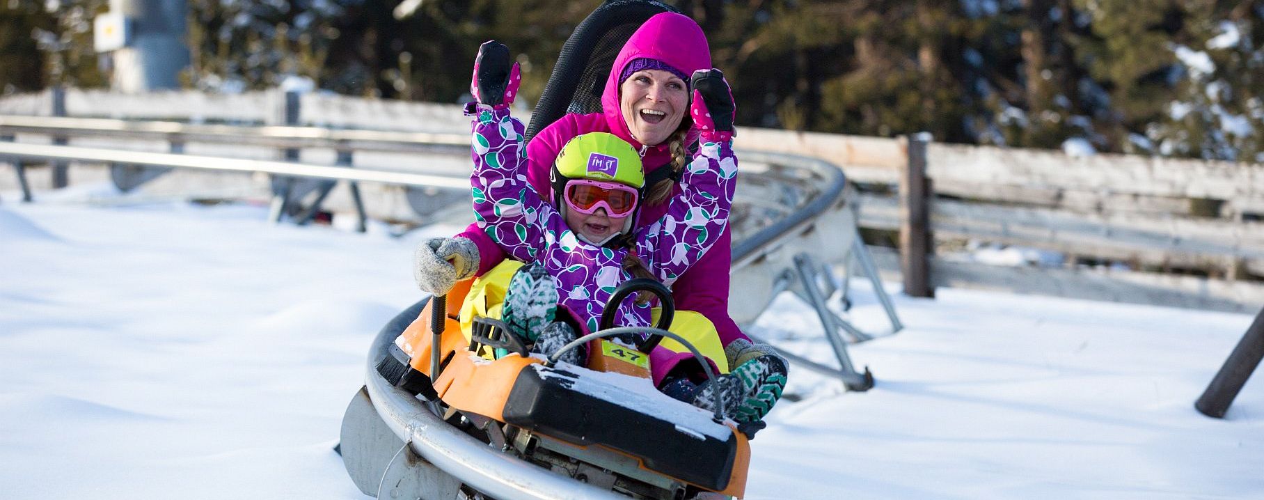 Eine Frau und ein Kind fahren im Winter im Alpine Coaster.