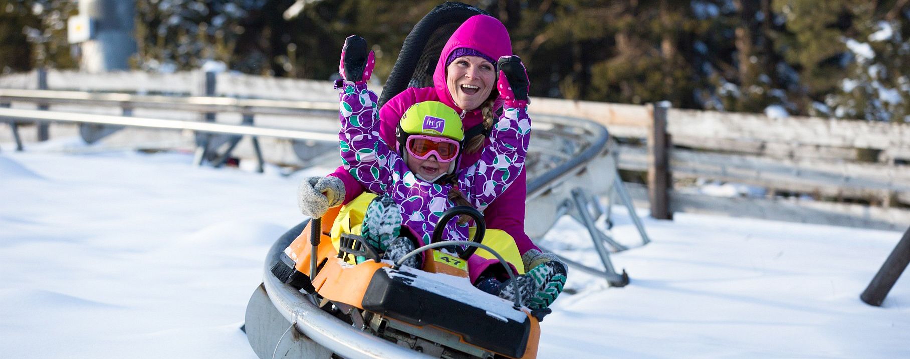 Eine Frau und ein Kind fahren im Winter im Alpine Coaster.