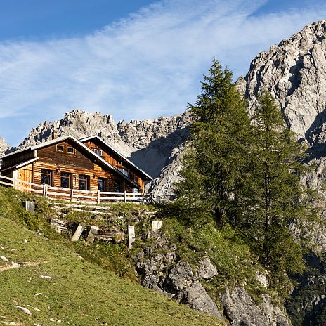 Eine Almhütte umringt von Bergen und blauer Himmel.