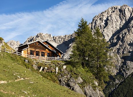 Eine Almhütte umringt von Bergen und blauer Himmel.