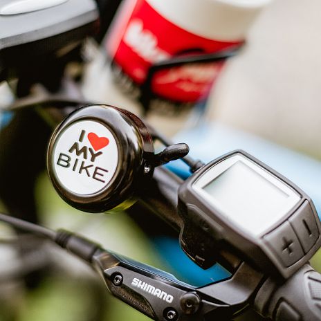 Nahaufnahme eines Fahrradlenkers mit einer Klingel, auf der "I love my bike" steht. Daneben ist ein elektronisches Display und ein Scheinwerfer zu sehen.
