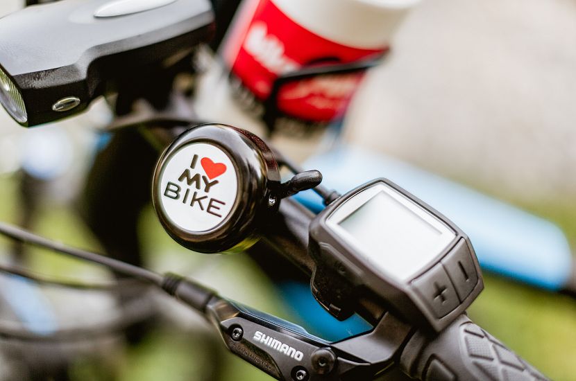 Nahaufnahme eines Fahrradlenkers mit einer Klingel, auf der "I love my bike" steht. Daneben ist ein elektronisches Display und ein Scheinwerfer zu sehen.